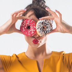 Young funny brunette model with donuts posing studio shot on white background, not isolated