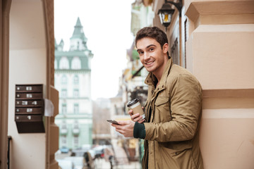 Cheerful man walking on street and chatting while drinking coffee