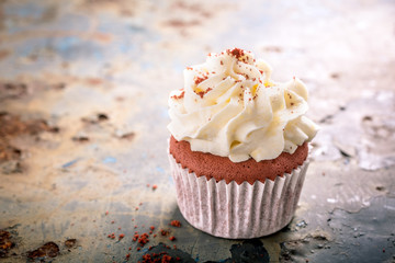 Delicious red velvet cupcake on rusty old metal background. Valentines Day greeting card concept with copy space. Retro style toned.