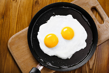 Two fried eggs in a frying pan cooked for breakfast. Delicious international meal on a table. Homemade food, top view.
