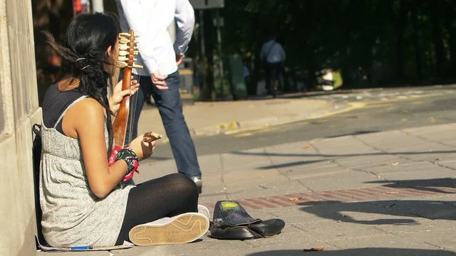 female beggar street artist playing on the sidewalk