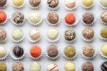 Chocolate truffle candies arranged in rows on white wooden background