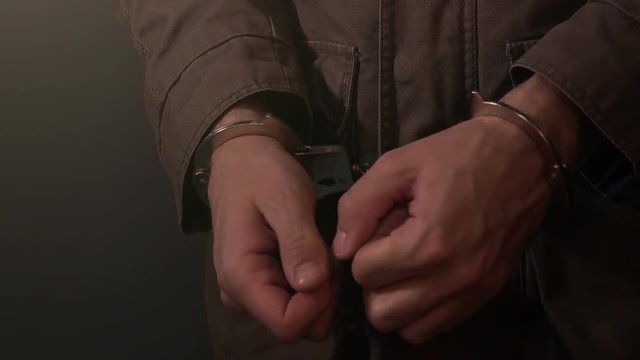 Arrested criminal, nervous cuffed male hands in dark prison room, close up