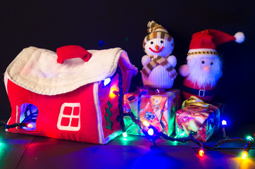 Новогодний Санта Клаус и снеговик рядом с домиком на тёмном фоне. Празднование Нового года. 