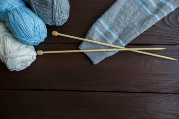 Knitting accessories: sleeve of grey with mint stripes knitted sweater, balls of yarn and needles for knitting on wooden background with copy space