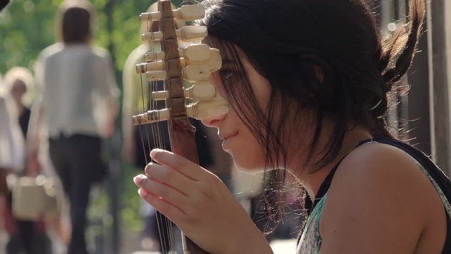 young woman playing string instrument on the sidewalk 