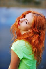 beautiful red-haired girl in a yellow shirt standing near water and stares dreamily