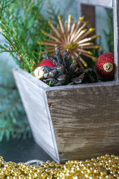 Christmas Basket with Vintage Gifts and Shining Candle. Red balls, Pine cones, Snowflakes, Boxes on Wooden Table. Warm Toned effect