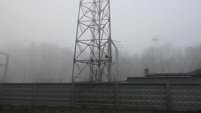Electricity constructions station in the dark foggy woods. Industrial area near the autumn or winter forest