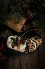 Traditional Christmas Baking: Stollen with dried fruits and nuts, sprinkled with powdered sugar. Miniature Christmas cake. Against the background of Christmas tree branches, cones and gifts 