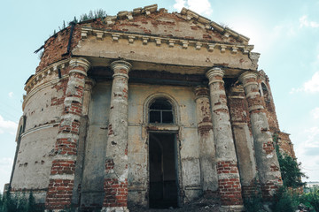old abandoned brick manor entrance with tall columns, overgrown with grass