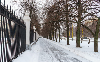 Fototapeta na wymiar The pedestrian walkway that runs along the iron palisade covered with snow in the winter in Moscow
