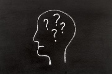 Hand drawing human head shape with chalk  on blackboard and question marks