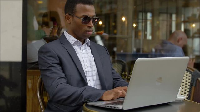 black elegant businessman working with his laptop sitting in a cafe in the city 