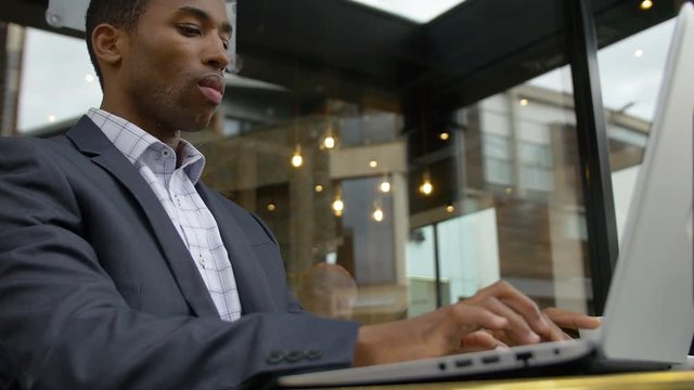 black elegant businessman working with his laptop sitting in a cafe in the city 