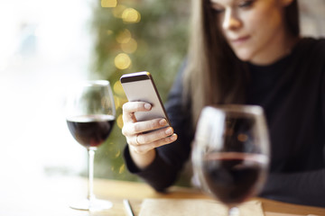 Woman using phone during lunch. Drinking glass of red wine in a