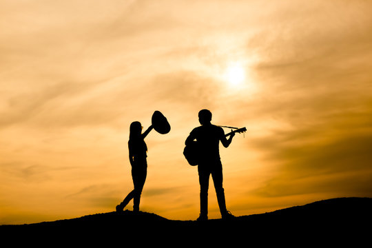 silhouette of musician with guitar and dancer at sunset
