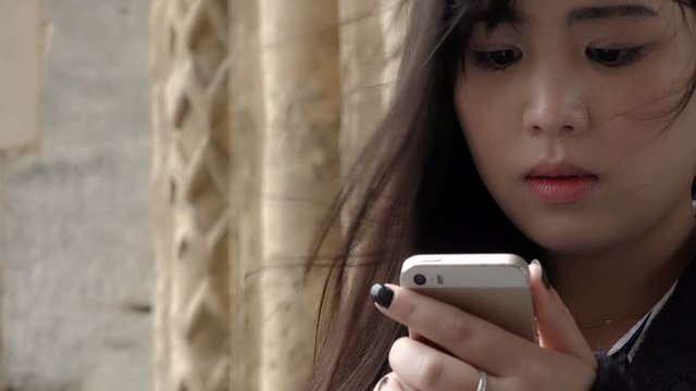 worried young chinese woman sending a short message with her smartphone