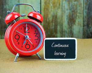 Continuous Learning inscription written on chalkboard, red alarm clock on desk with old wooden...