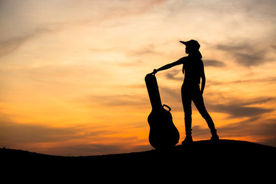 Silhouette of woman with guitar on the sunset