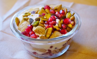 A breakfast yogurt parfait with pomegranates and pistachio nuts in a glass jar