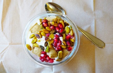 A breakfast yogurt parfait with pomegranates and pistachio nuts in a glass jar