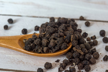 Closeup view of black pepper corns and spoon  on white wooden background
