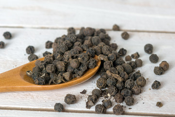 Closeup view of black pepper corns and spoon  on white wooden background
