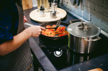 woman housewife prepares fried eggs with ham and vegetables in his kitchen. stir peppers and tomatoes in a pan