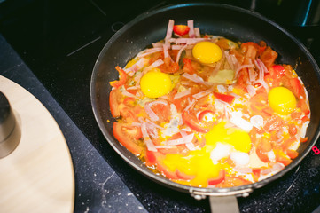 woman housewife prepares fried eggs with ham and vegetables in his kitchen. egg breaks, adding to the pan