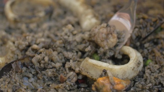 Close-up shot of a person eating black paella with seafood such as calamars and mussels. Spanish cuisine