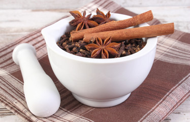 Fragrant cloves, anise and cinnamon in mortar on rustic board
