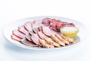 Assorted meat: ham, smoked sausage, salami, chicken, tongue and mustard on a white background