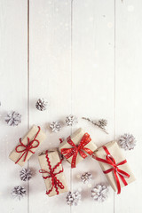 Fototapeta na wymiar Gift boxes with red ribbons and pine cones on a white wooden tab