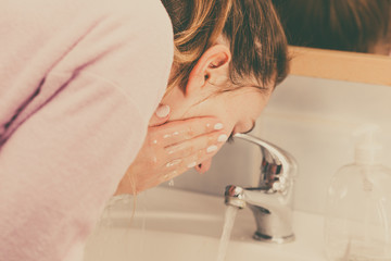 Woman washing face in bathroom. Hygiene.
