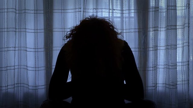 woman in yoga pose in a dark room seems to be reproaching herself