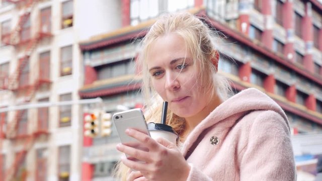 Young tourist drink bubble tea in Chinatown New York, USA. She uses a smartphone