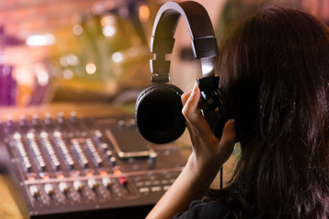 Woman  holding headphone and  listening live sound .Producer adjusting and balancing audio input to digital mixer  in live concert,bokeh and blurred background of drum kit