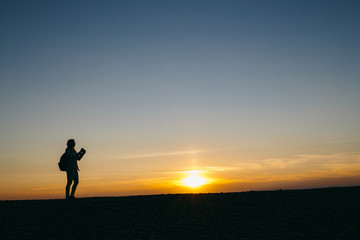 silhouette of a young woman taking pictures on the camera at sunset background