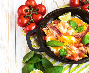 Pan of fried eggs with tomatoes, bacon, spinach, lime