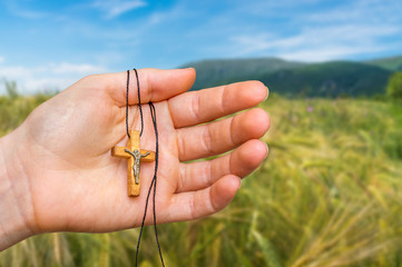 Female hand with wooden cross on rye field background