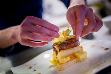 Chef composing a dish with a beef fillet and some potato chips