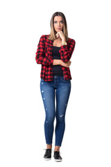 Gorgeous pensive casual woman in red checkered shirt with hands on chin looking at camera. Full body length standing portrait isolated over white background.