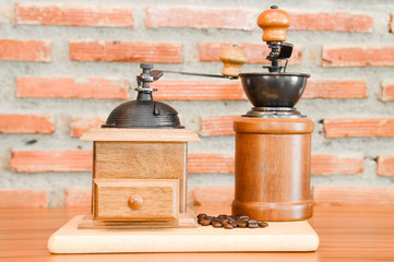 Coffee grinder with coffee beans on wooden table with brick back