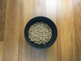 Peeled sunflower seeds in a black cup on wood background,top vie