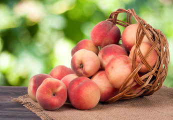 peaches in a wicker basket on wooden table with blurred background