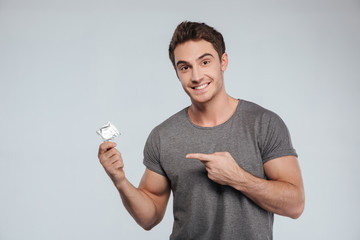Portrait of a young smiling man pointing finger at condom - obrazy, fototapety, plakaty