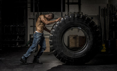 Fototapeta na wymiar Muscle Man in Jeans Pushing Large Tire