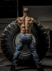 Fototapeta na wymiar Muscle Man in Jeans holding Large Tire 