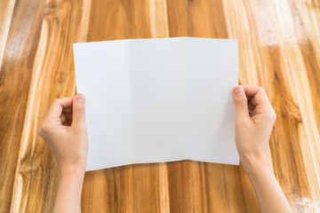 Obraz premium Women hand hold Trifold white template paper on wood texture .